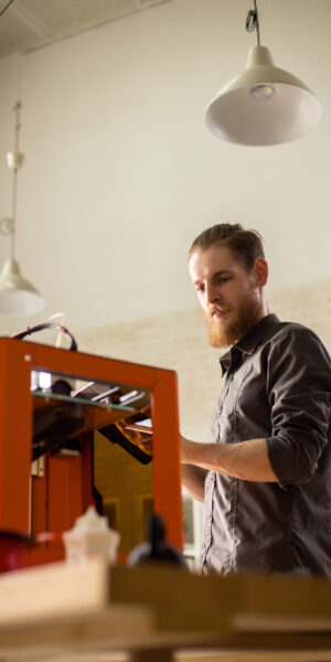 Working on Ambitious Project Low angle view of handsome bearded designer using 3D printer while working on ambitious project, interior of modern studio on background